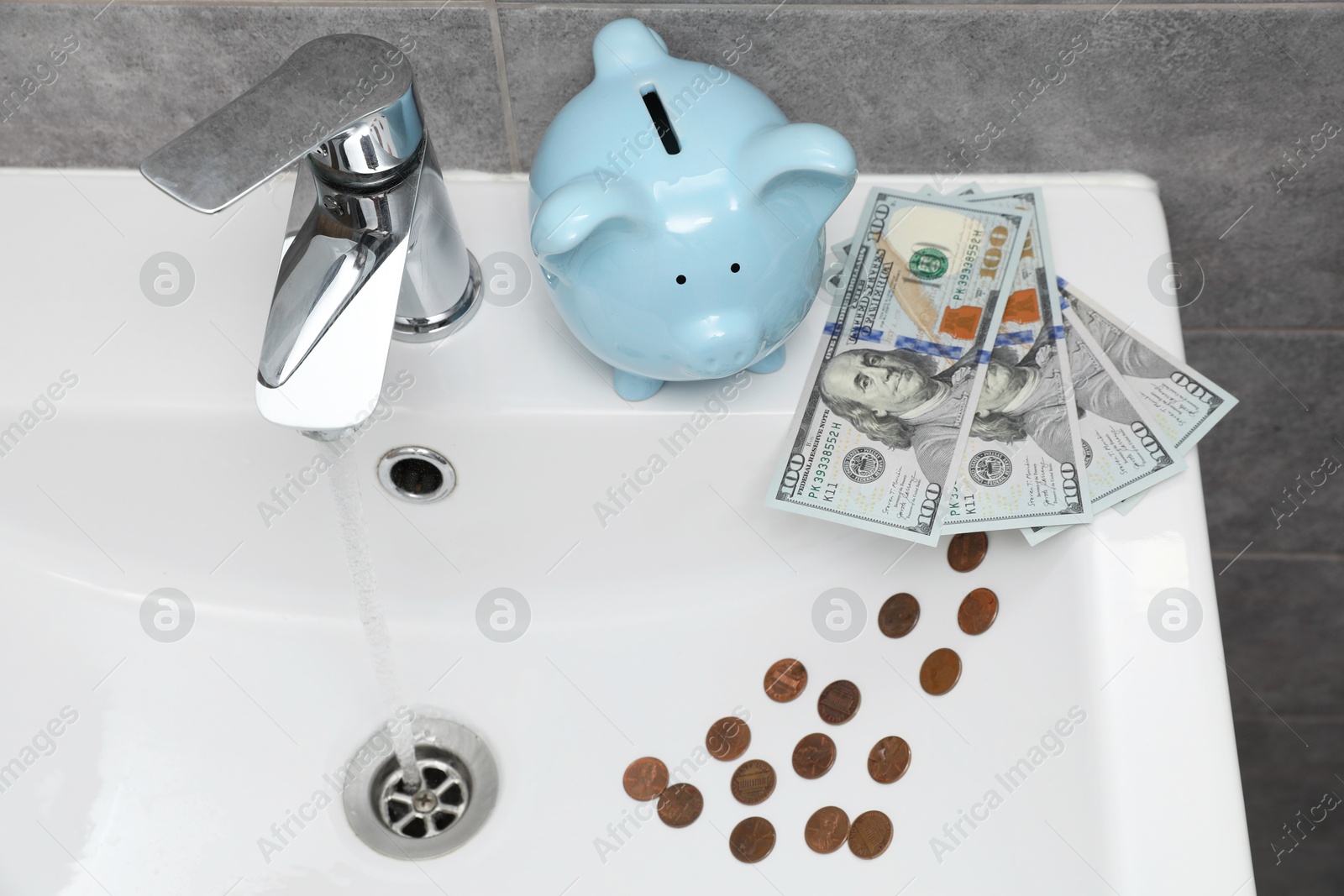Water saving concept. Piggy bank, stream of water flowing from tap and money in bathroom Photo of Water saving concept. Piggy bank, stream of water flowing from tap and money in bathroom