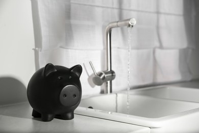 Photo of Water saving concept. Piggy bank and stream of water flowing from tap in kitchen