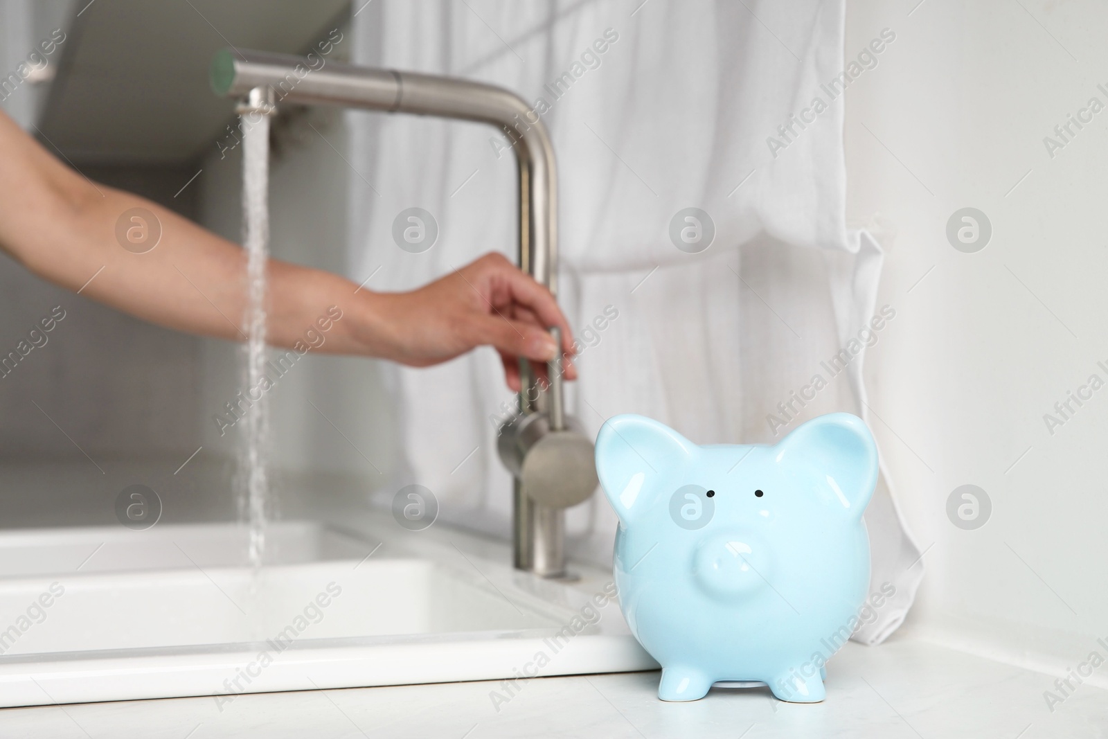 Water saving concept. Woman checking water flow in kitchen, focus on piggy bank Photo of Water saving concept. Woman checking water flow in kitchen, focus on piggy bank