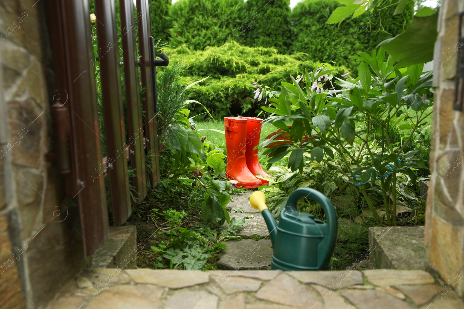 Photo of Orange rubber boots and watering can outdoors