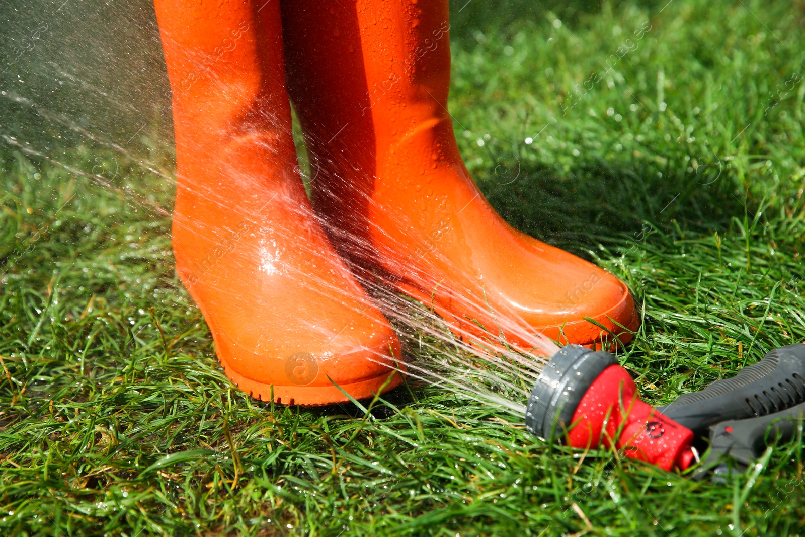 Photo of Orange rubber boots under water pressure on green grass outdoors