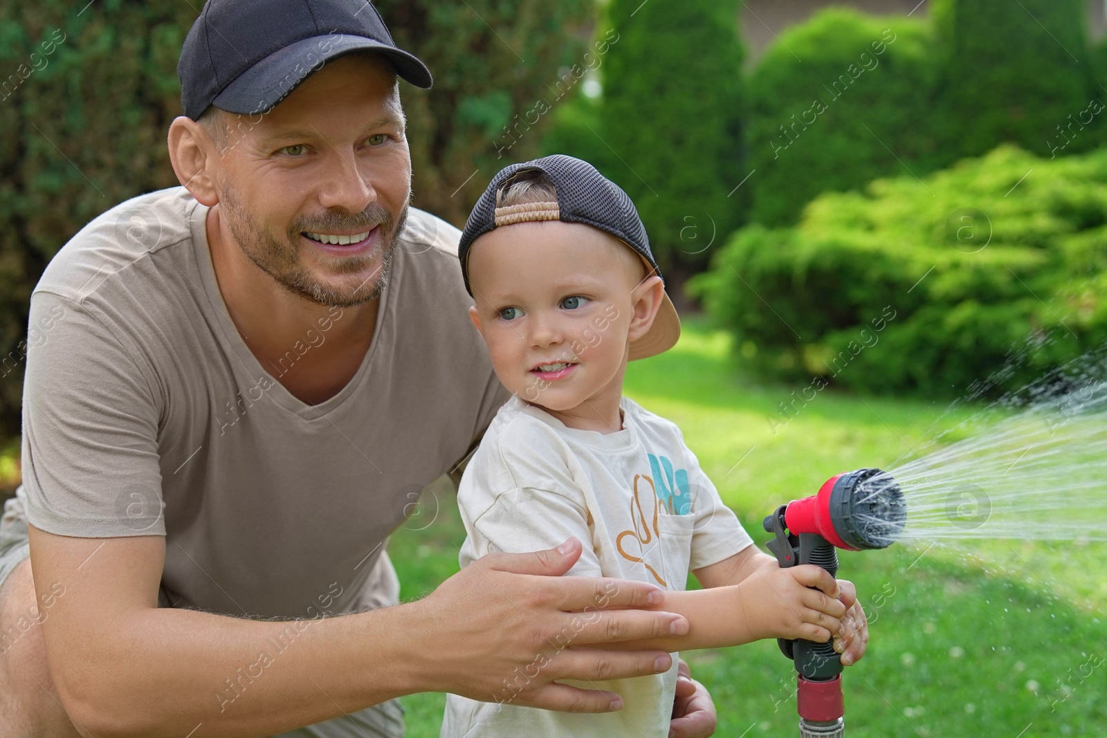 Photo of Father and his son watering lawn with hose in backyard