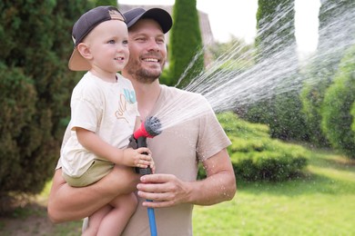 Photo of Father and his son watering lawn with hose in backyard