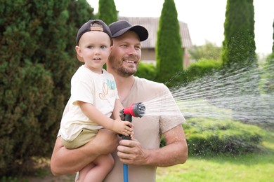 Photo of Father and his son watering lawn with hose in backyard