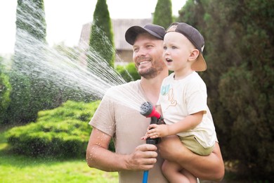 Photo of Father and his son watering lawn with hose in backyard