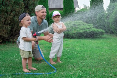 Photo of Father and his kids watering lawn with hose in backyard