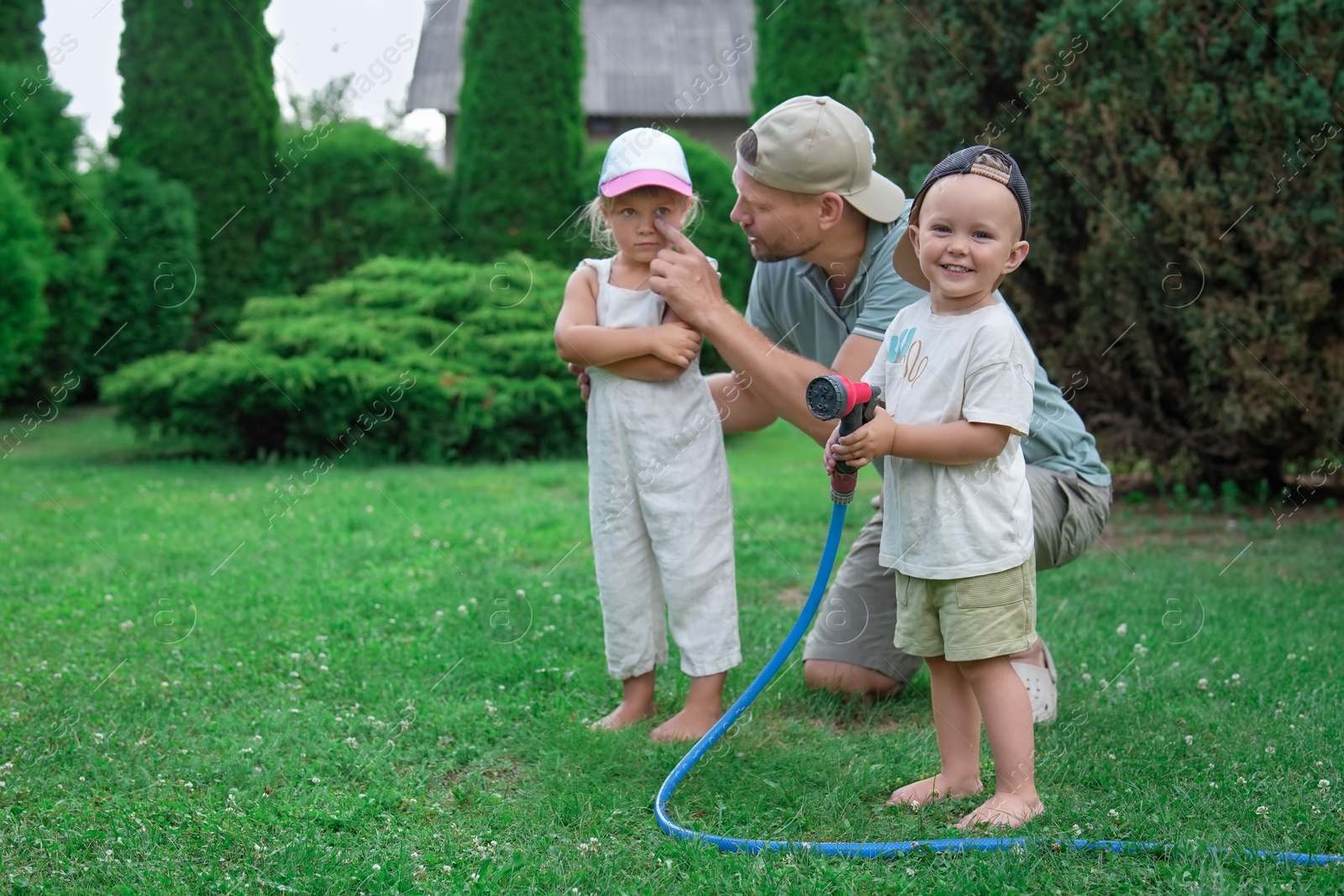 Photo of Father and his kids watering lawn with hose in backyard, space for text