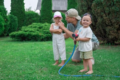 Father and his kids watering lawn with hose in backyard, space for text