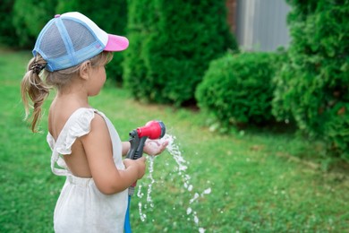 Little girl watering lawn with hose in backyard, space for text