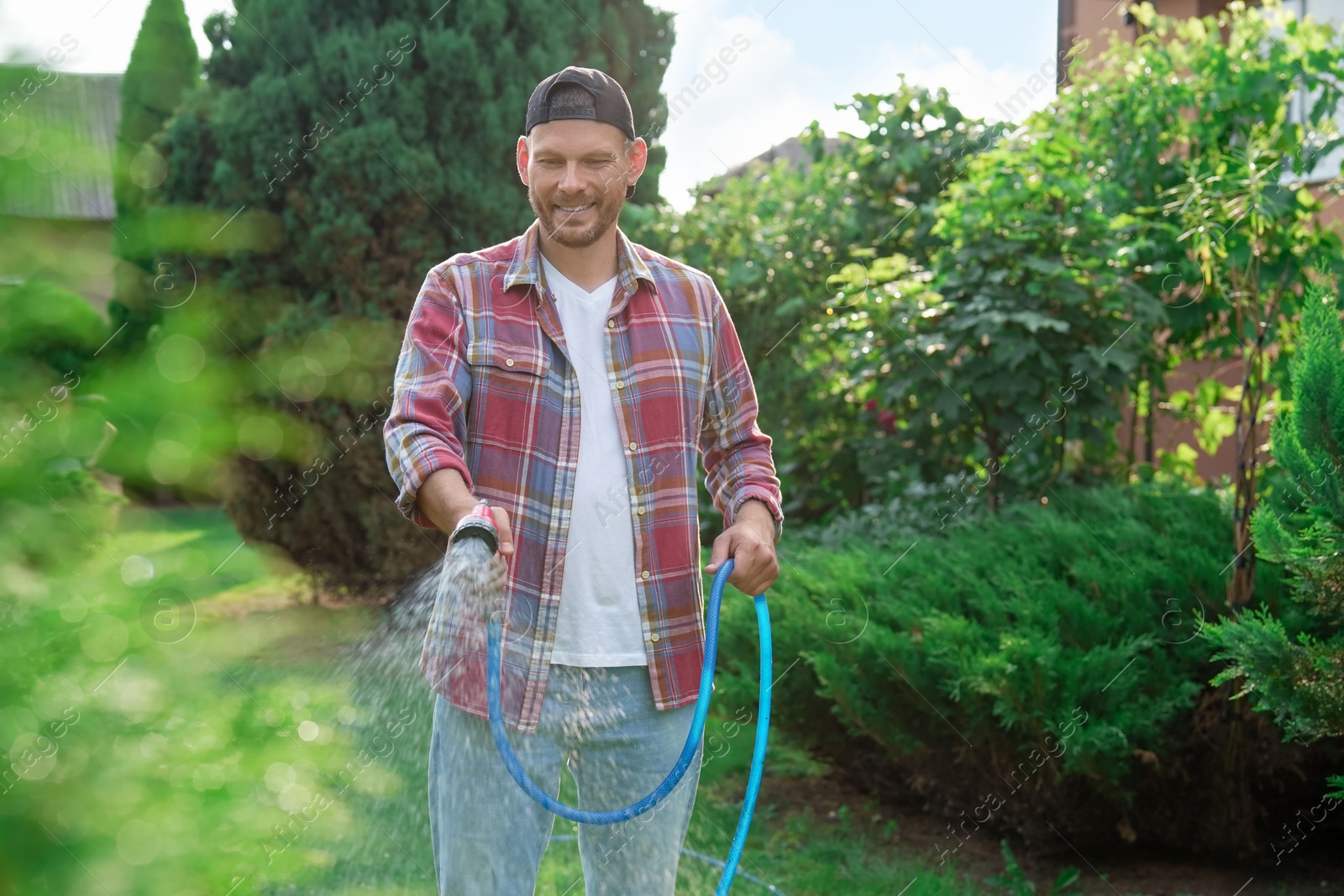 Photo of Man watering lawn with hose in backyard