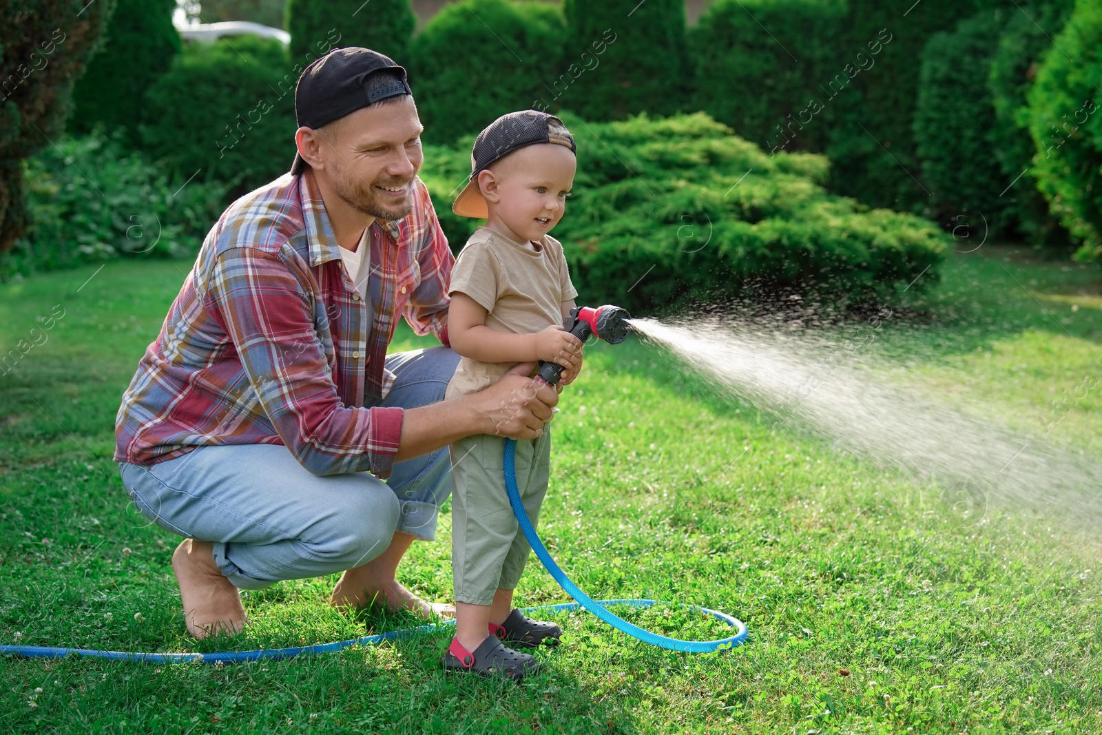 Photo of Father and his son watering lawn with hose in backyard