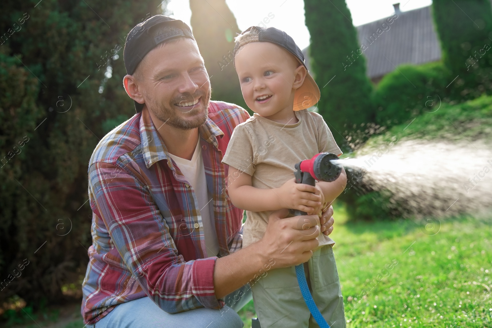 Photo of Father and his son watering lawn with hose in backyard