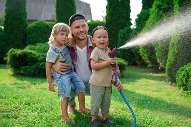 Photo of Father and his kids watering lawn with hose in backyard