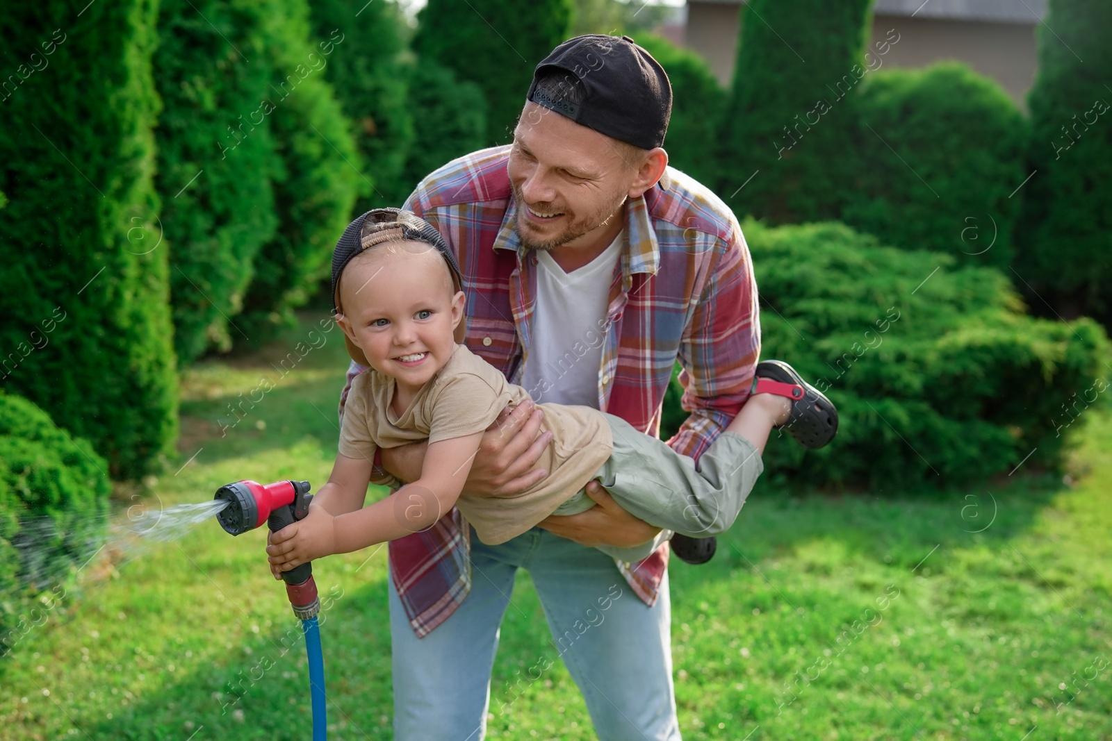 Photo of Father and his son watering lawn with hose in backyard