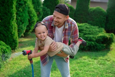 Father and his son watering lawn with hose in backyard