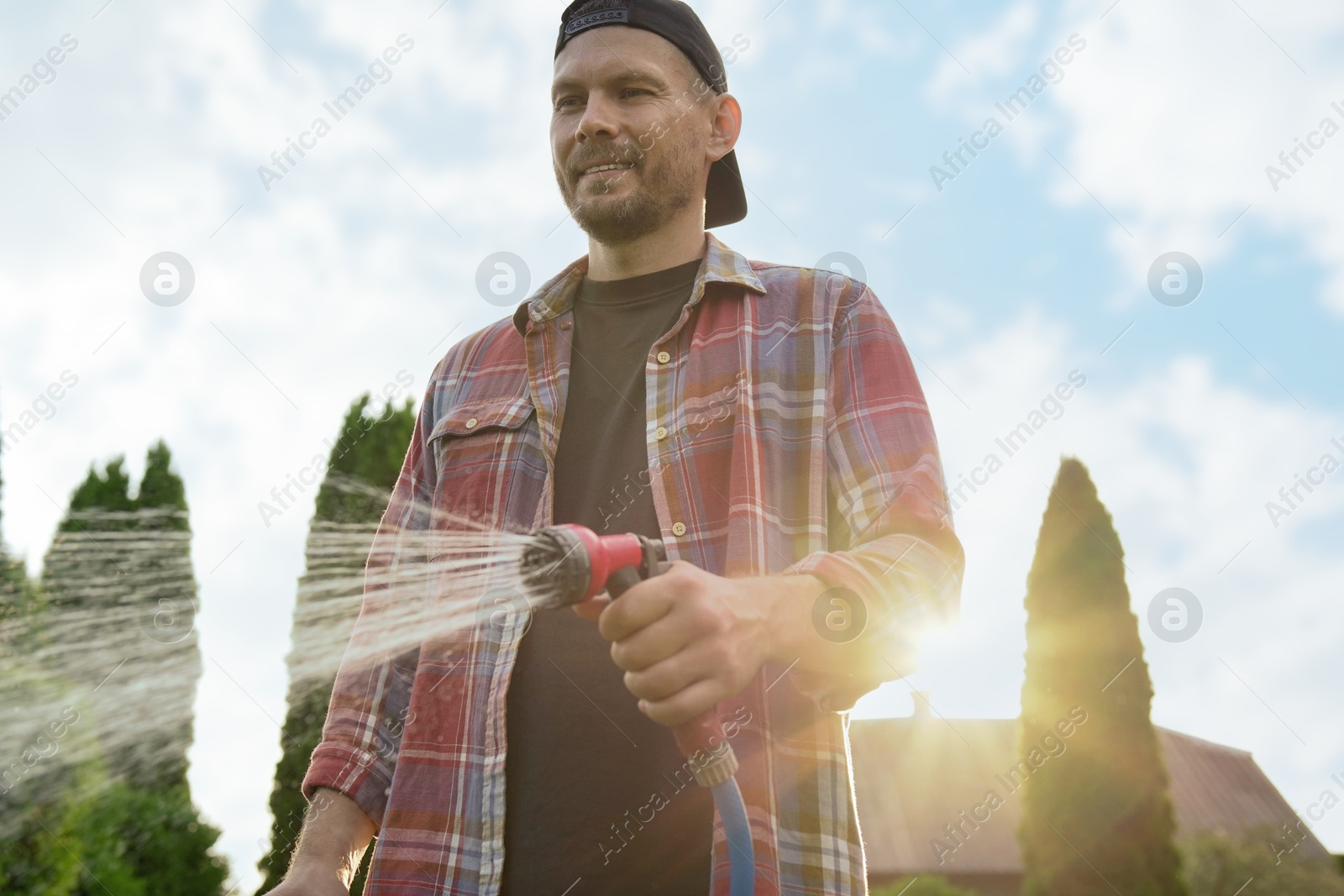 Photo of Man watering lawn with hose in backyard