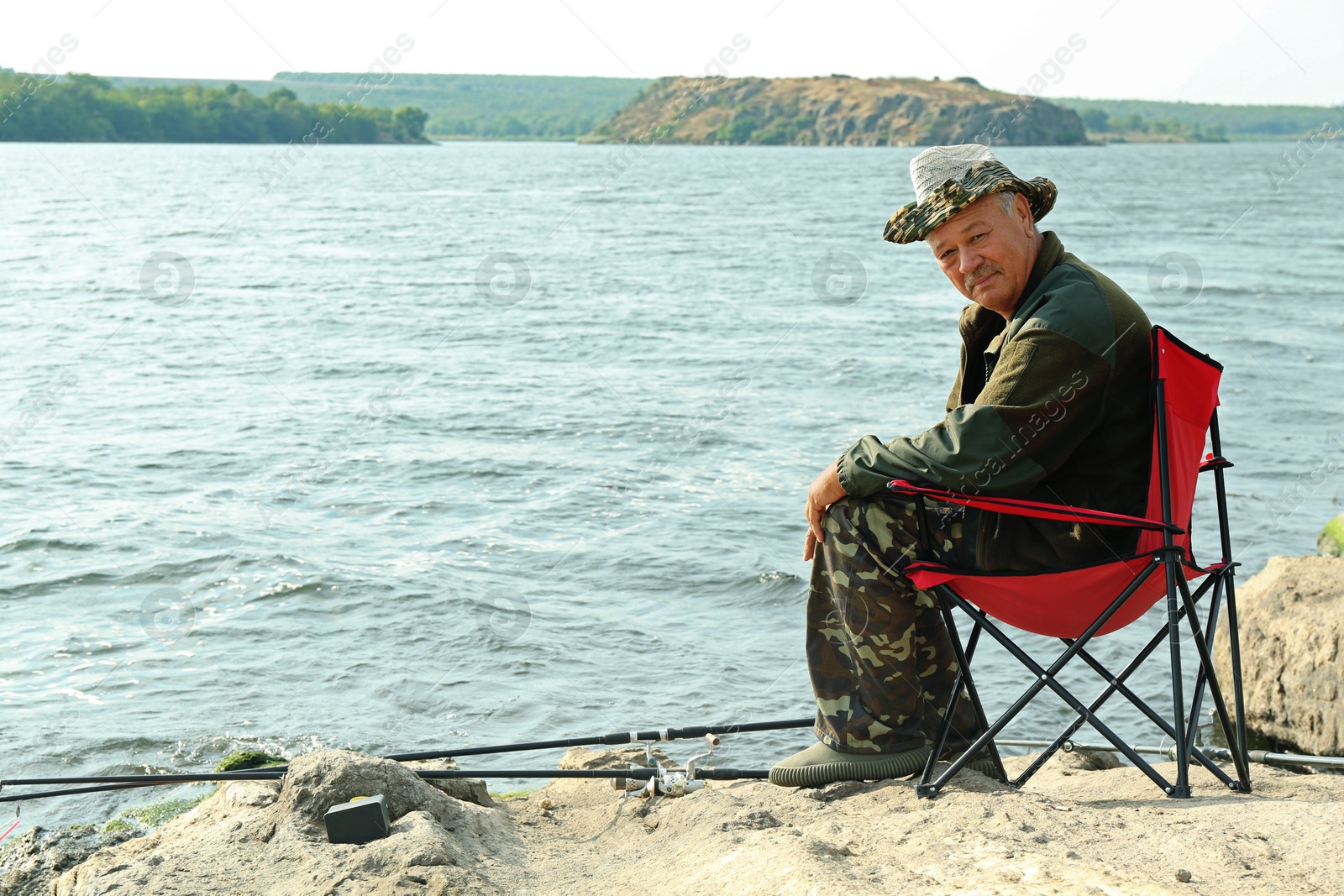 Photo of Fisherman with rod sitting on chair and fishing near lake at summer, space for text