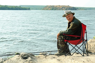 Fisherman with rod sitting on chair and fishing near lake at summer, space for text