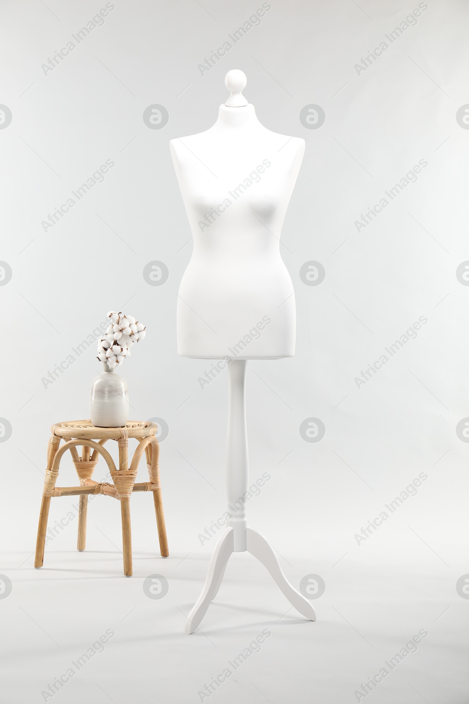 Photo of One female mannequin on stand, stool and vase with cotton flowers against light background