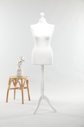 Photo of One female mannequin on stand, stool and vase with cotton flowers against light background