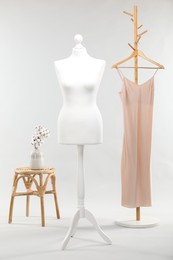 Photo of One female mannequin on stand, rack with dress, stool and cotton flowers in vase against light background