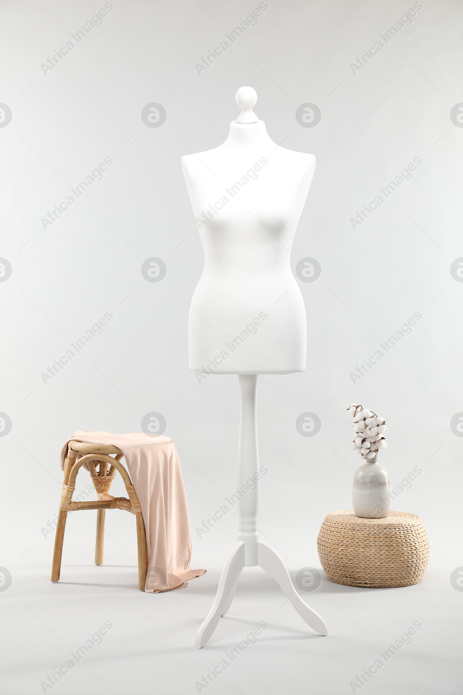 Photo of One female mannequin on stand, stool, pouf and vase with cotton flowers against light background