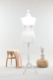 One female mannequin on stand, stool, pouf and vase with cotton flowers against light background