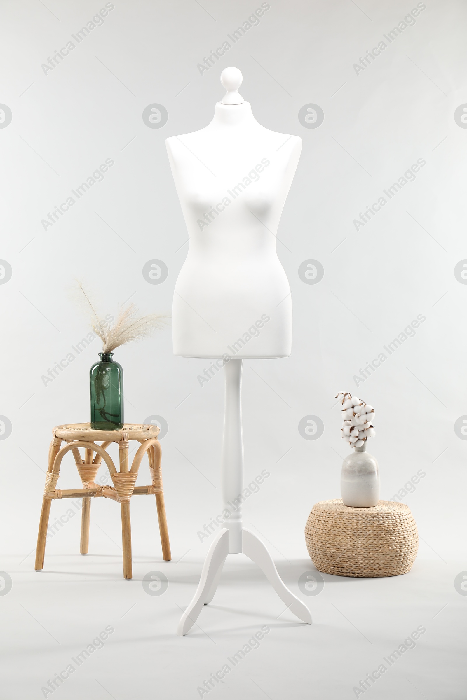 Photo of One female mannequin on stand, stool, pouf and vases with plants against light background