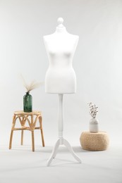 Photo of One female mannequin on stand, stool, pouf and vases with plants against light background