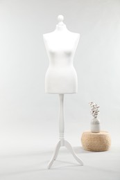 Photo of One female mannequin on stand, pouf and vase with cotton flowers against light background