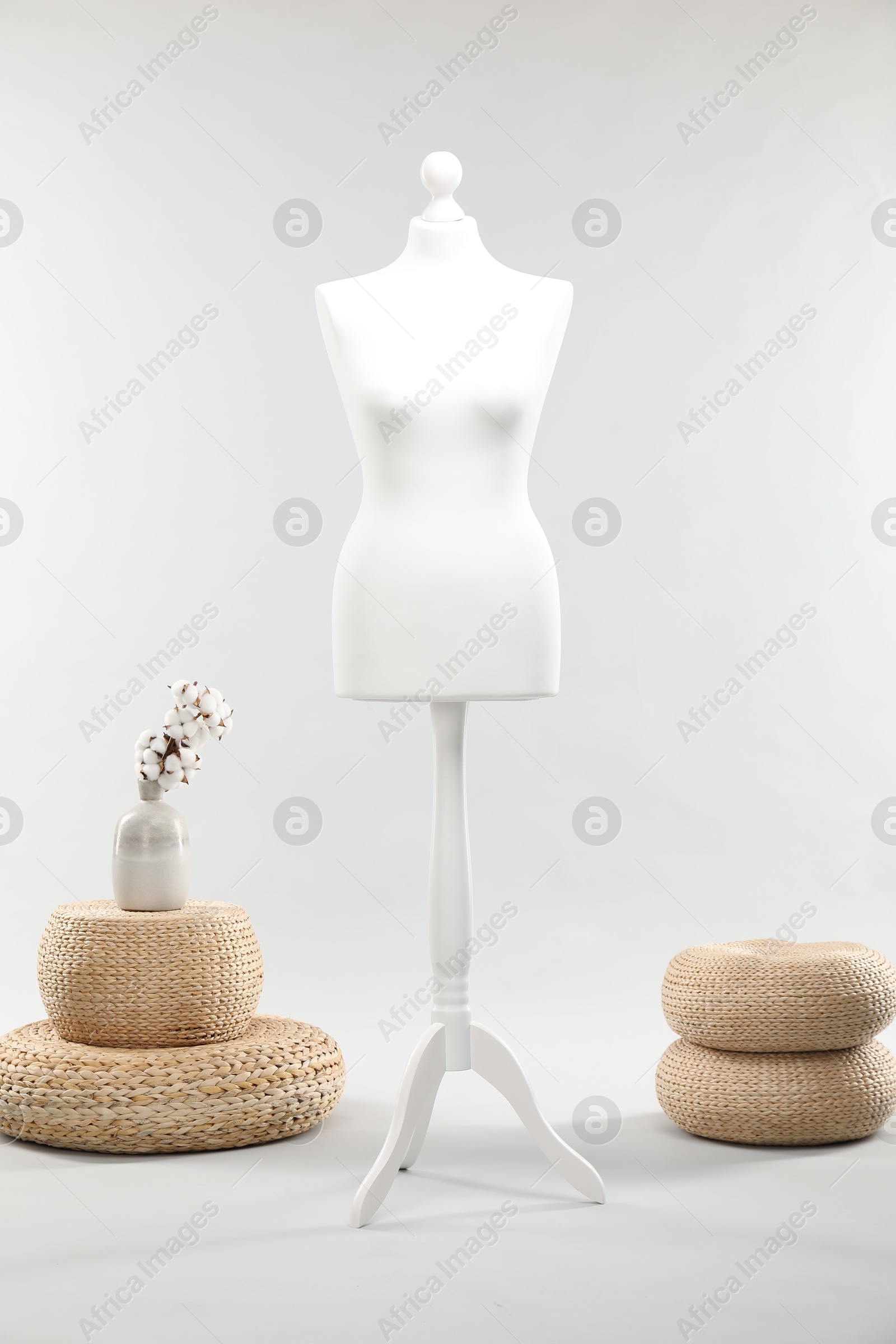 Photo of One female mannequin on stand, poufs and vase with cotton flowers against light background