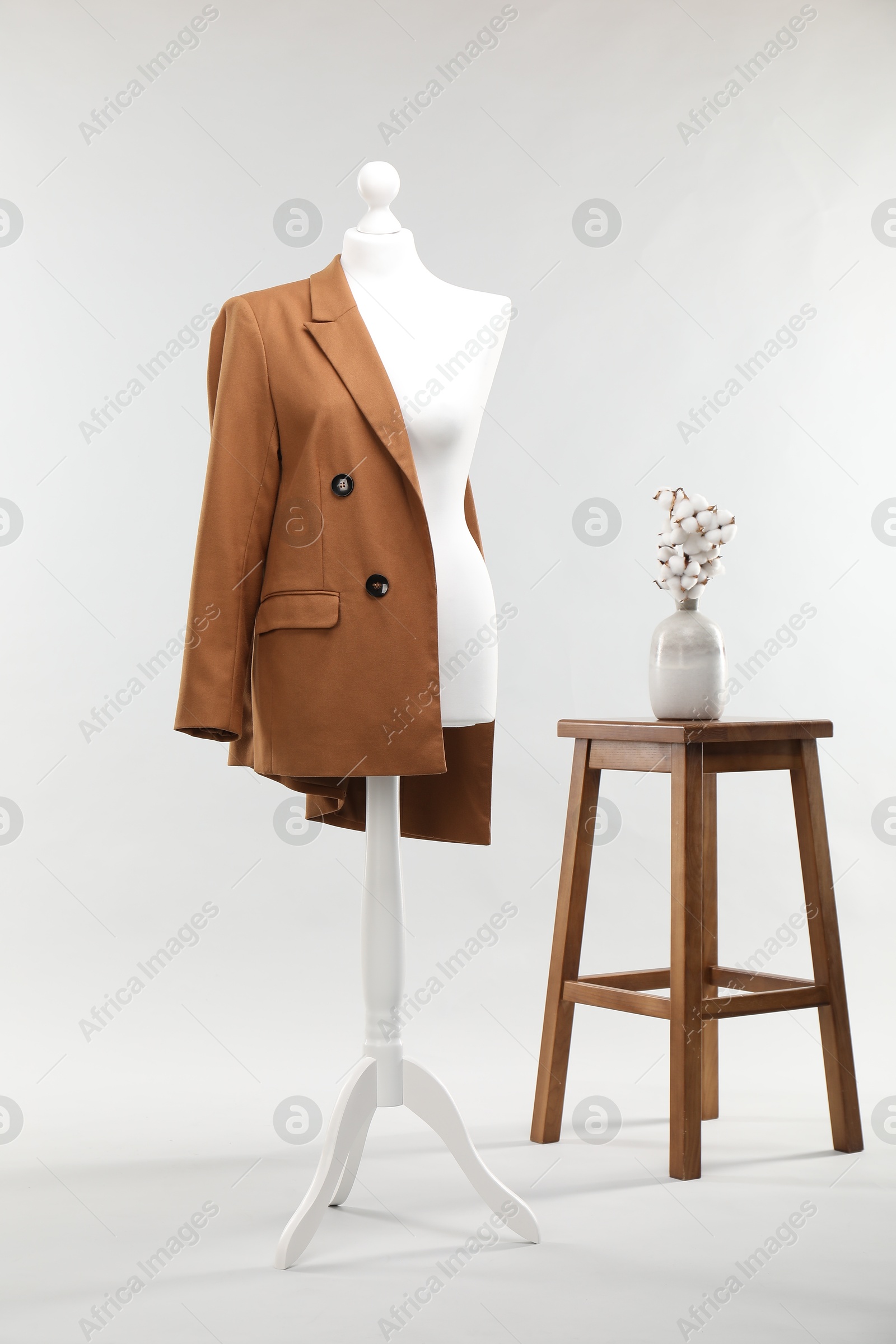 Photo of One female mannequin with jacket, stool and cotton flowers on light background