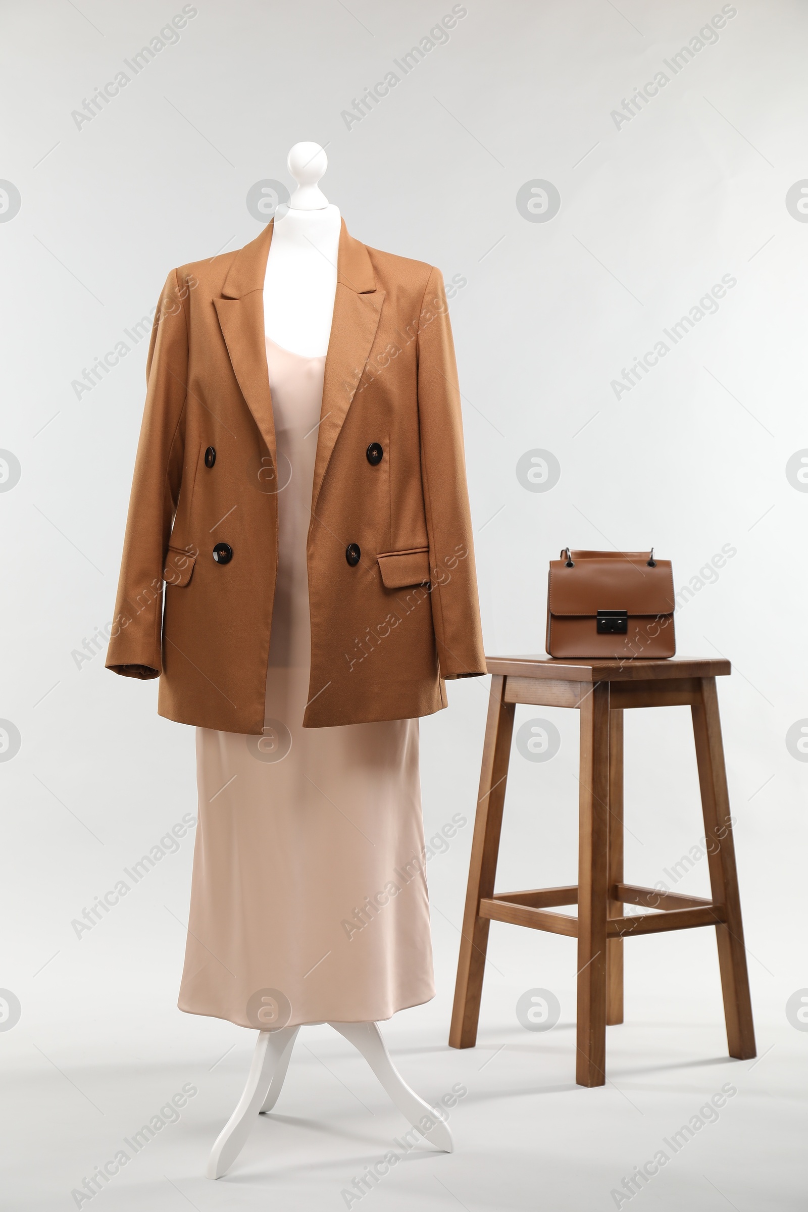 Photo of One female mannequin with dress, jacket, stool and bag on light background