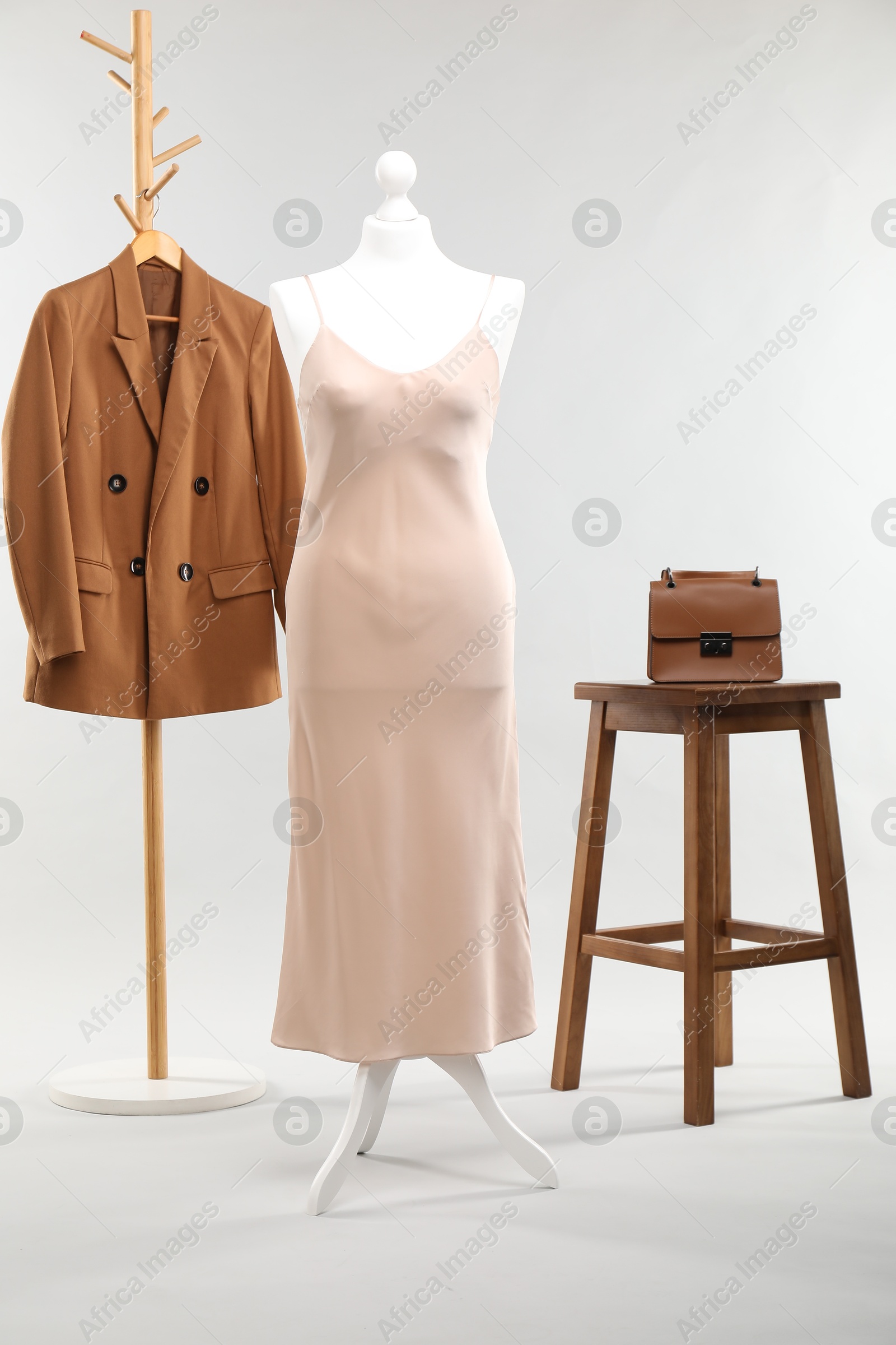 Photo of One female mannequin with dress, rack with jacket, stool and bag on light background