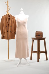 One female mannequin with dress, rack with jacket, stool and bag on light background