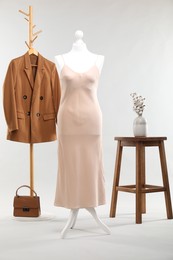 One female mannequin with dress, rack with jacket, stool, cotton flowers and bag on light background