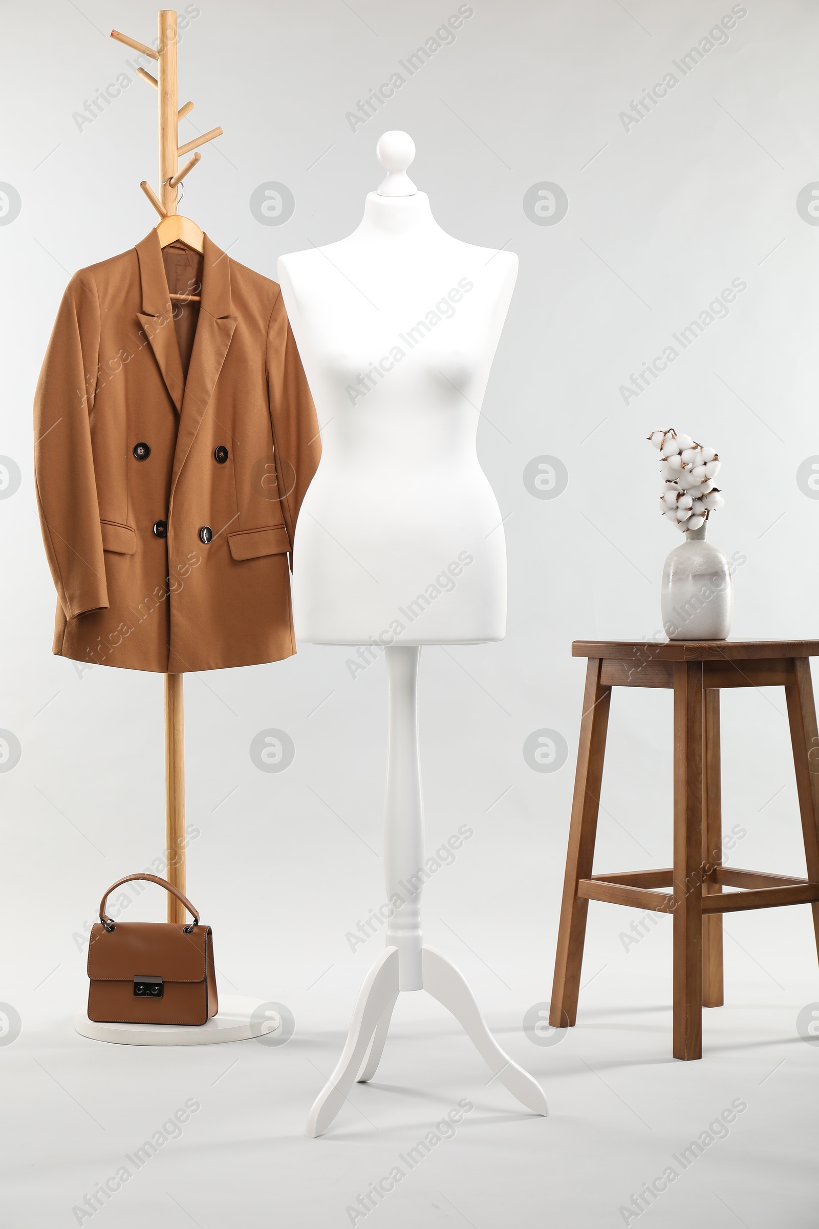 Photo of One female mannequin, rack with jacket, stool, cotton flowers and bag on light background