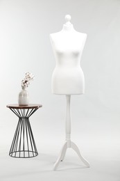 One female mannequin and coffee table with cotton flowers on light background