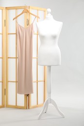 One female mannequin and folding screen with dress on light background