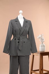 Female mannequin with suit, stool and cotton flowers on beige background