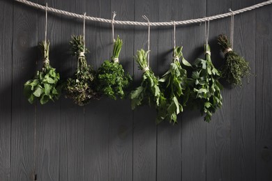 Photo of Bunches of different aromatic herbs hanging on rope near grey wooden wall