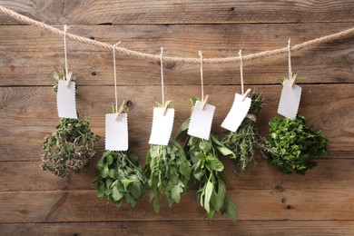 Photo of Bunches of different aromatic herbs with blank notes hanging on rope near wooden wall