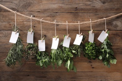 Photo of Bunches of different aromatic herbs with blank notes hanging on rope near wooden wall