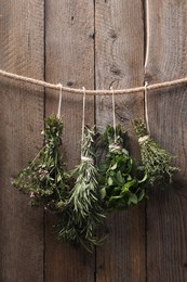 Photo of Bunches of different aromatic herbs hanging on rope near wooden wall