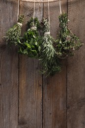 Photo of Bunches of different aromatic herbs hanging on rope near wooden wall