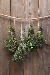 Photo of Bunches of different aromatic herbs hanging on rope near wooden wall