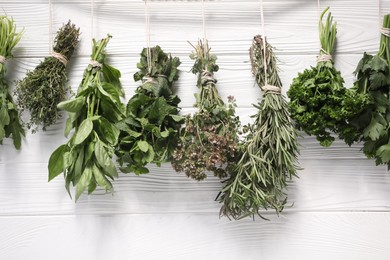 Photo of Bunches of different aromatic herbs hanging on rope near white wooden wall