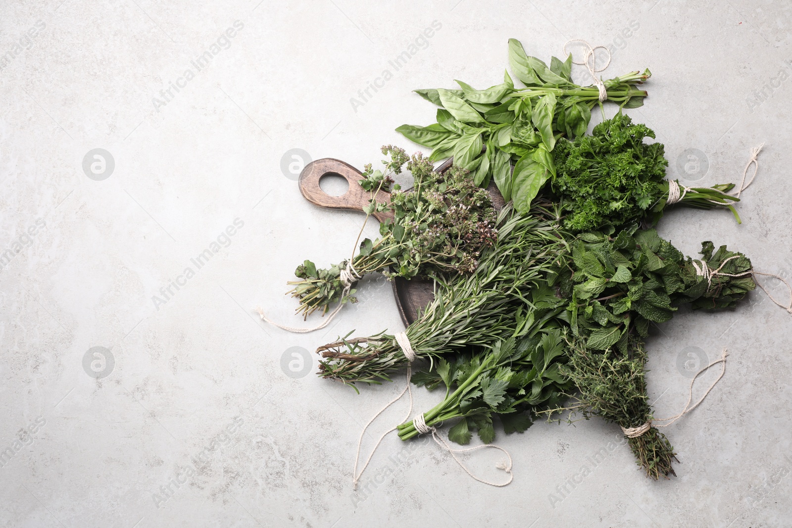 Photo of Bunches of different aromatic herbs on grey textured table, top view. Space for text