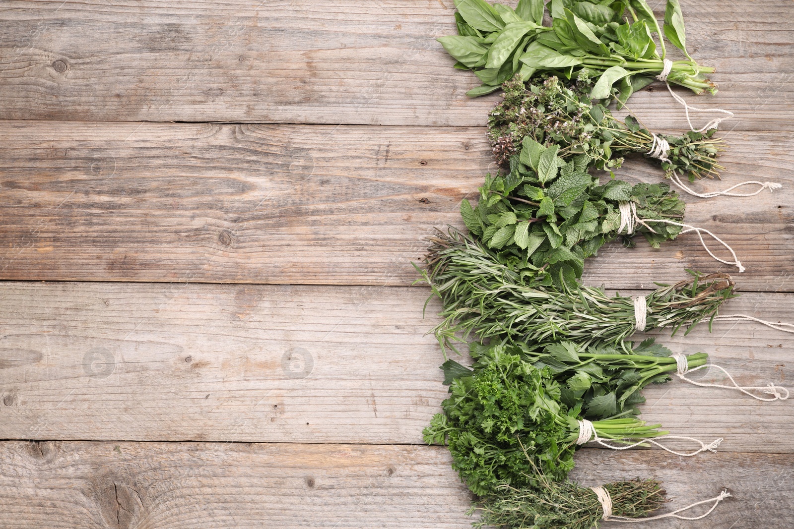 Photo of Bunches of different aromatic herbs on wooden table, flat lay. Space for text