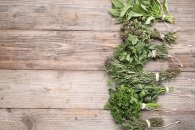 Photo of Bunches of different aromatic herbs on wooden table, flat lay. Space for text